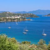 A high angle shot of sailing ships on the ocean near grassy hills in Skiathos Greece on a sunny day